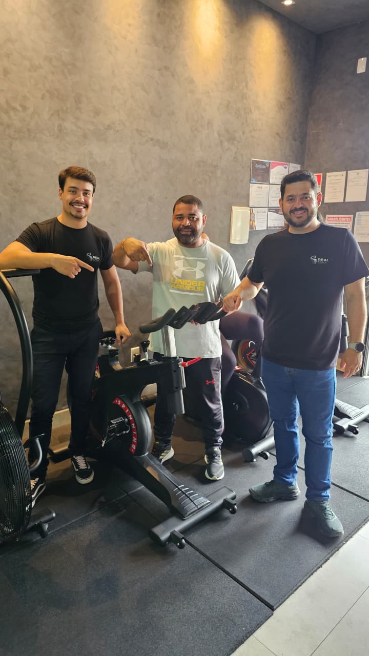 Equipe comercial da Real Force Fitness com o cliente do Studio David Brito, em Cristalina-GO, ao lado de bicicleta de spinning